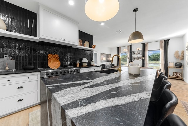 kitchen with dark stone counters, light wood-type flooring, sink, hanging light fixtures, and a spacious island