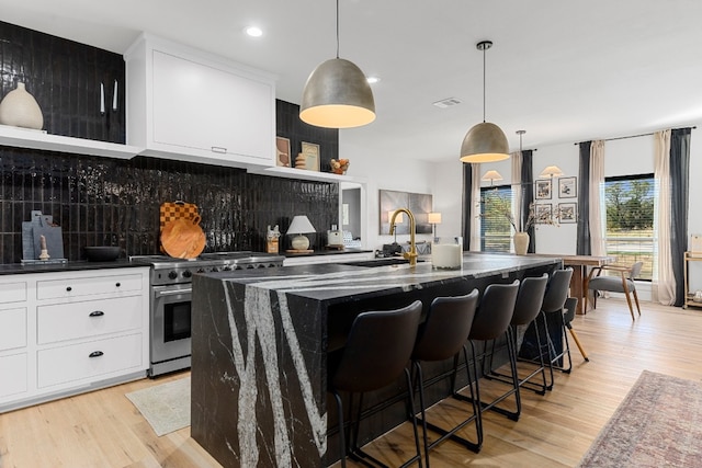 kitchen featuring sink, high end range, light hardwood / wood-style flooring, a kitchen island with sink, and decorative backsplash