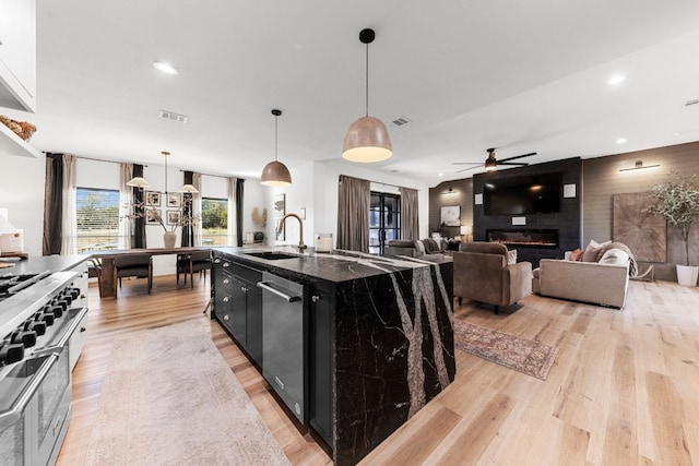 kitchen featuring sink, a center island with sink, decorative light fixtures, appliances with stainless steel finishes, and a large fireplace