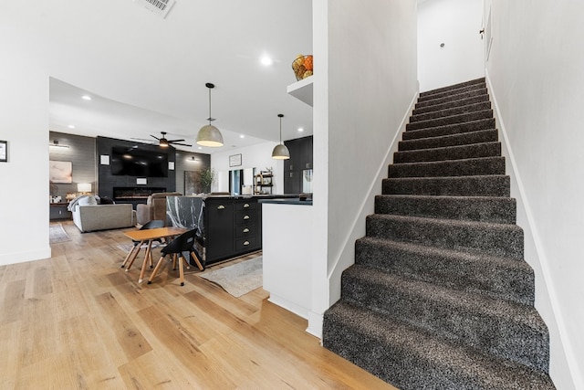 stairway with hardwood / wood-style floors, a large fireplace, and ceiling fan