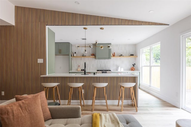 bar featuring backsplash, sink, green cabinetry, decorative light fixtures, and light hardwood / wood-style floors