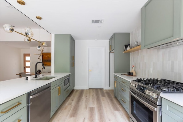 kitchen featuring appliances with stainless steel finishes, light wood-type flooring, backsplash, sink, and decorative light fixtures