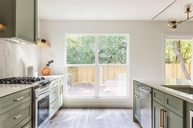 kitchen featuring light wood-type flooring, tasteful backsplash, stainless steel appliances, sink, and green cabinetry