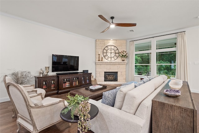 living room featuring ceiling fan, crown molding, hardwood / wood-style floors, and a stone fireplace