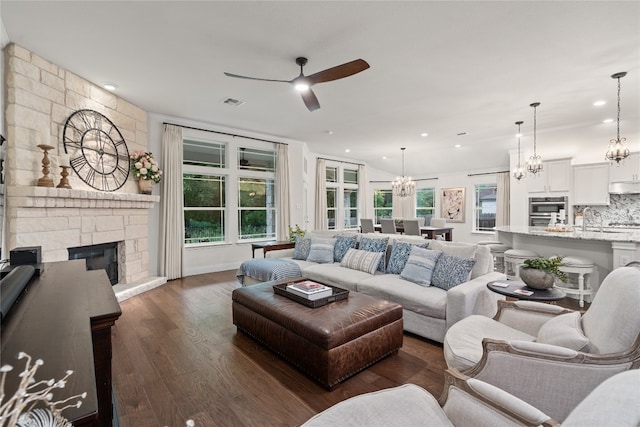 living room with a healthy amount of sunlight, a fireplace, ceiling fan with notable chandelier, and dark wood-type flooring