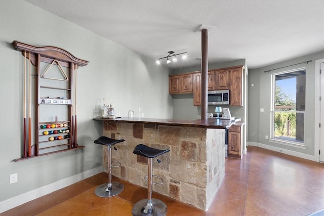 4408 Blacksmith Cv, Spicewood, TX 78669 - kitchen featuring stainless steel microwave, brown cabinetry, concrete flooring, a peninsula, and a kitchen bar