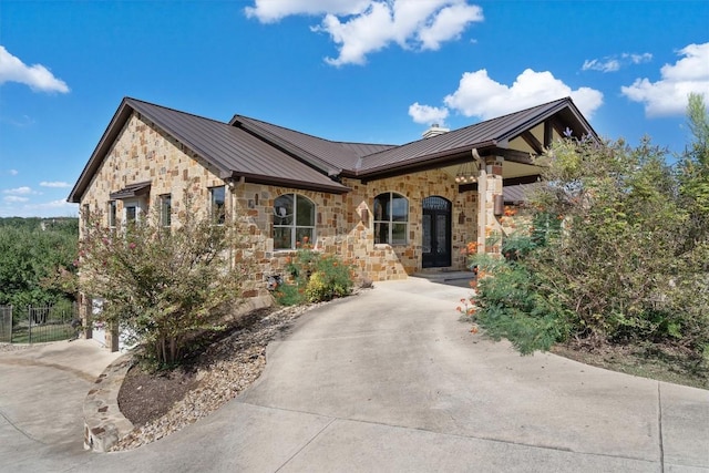 single story home with a standing seam roof, metal roof, concrete driveway, and stone siding