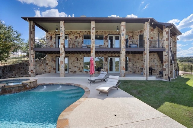 back of house featuring a pool with connected hot tub, a lawn, a patio, stone siding, and french doors