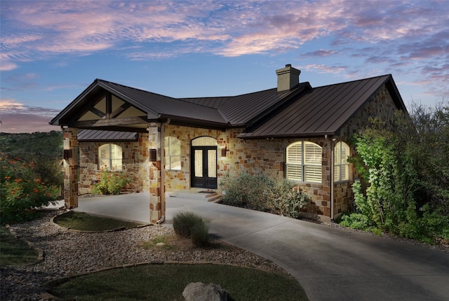 4408 Blacksmith Cv, Spicewood, TX 78669 - view of front facade featuring a standing seam roof, a chimney, stone siding, and a metal roof