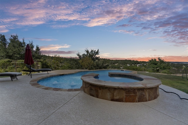 pool at dusk with a patio and a pool with connected hot tub