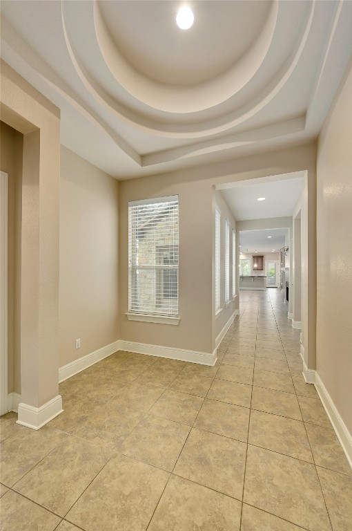 hallway featuring a tray ceiling, a wealth of natural light, and light tile patterned floors