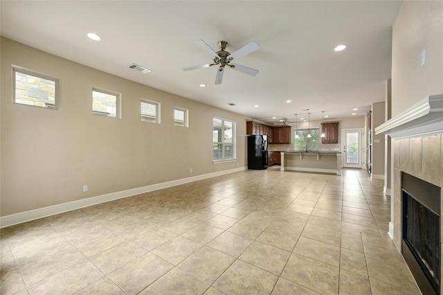 unfurnished living room with ceiling fan, light tile patterned floors, and a tile fireplace