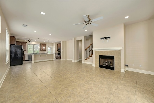 unfurnished living room with ceiling fan, sink, light tile patterned floors, and a fireplace