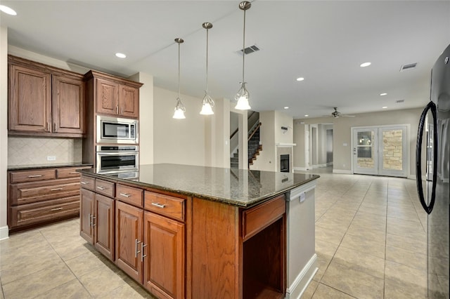 kitchen featuring ceiling fan, hanging light fixtures, dark stone counters, a kitchen island, and appliances with stainless steel finishes