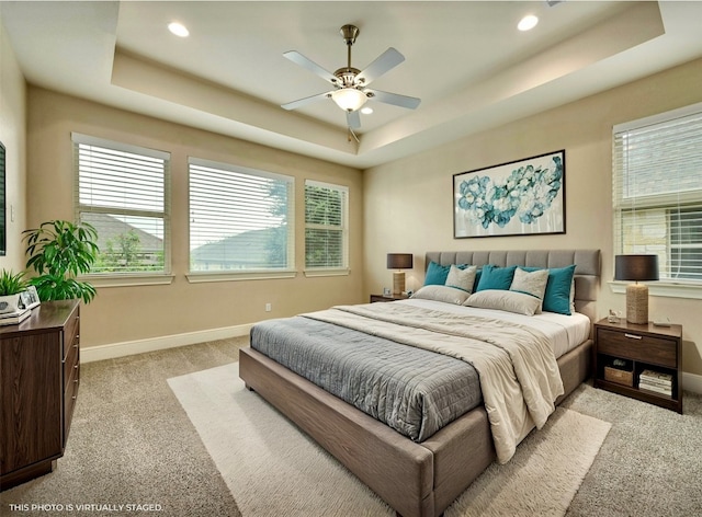 bedroom featuring ceiling fan, light colored carpet, and a tray ceiling