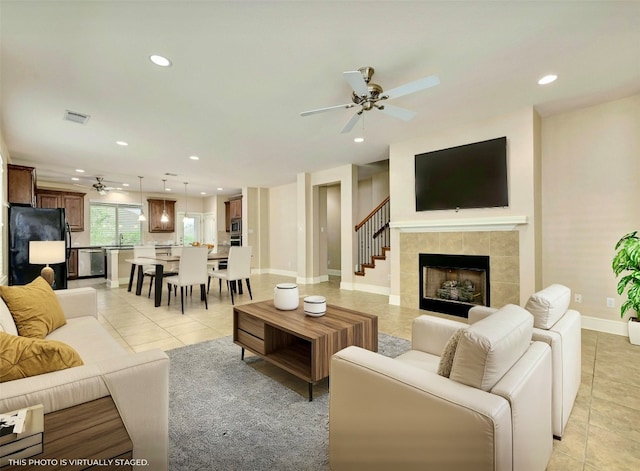 tiled living room with ceiling fan, sink, and a tile fireplace