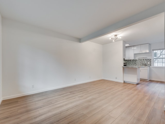 unfurnished living room featuring an inviting chandelier, beam ceiling, and light hardwood / wood-style floors