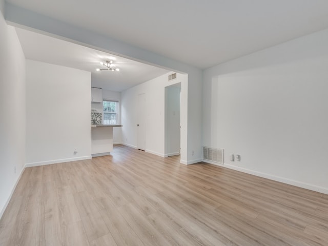 empty room featuring light wood-type flooring and a notable chandelier