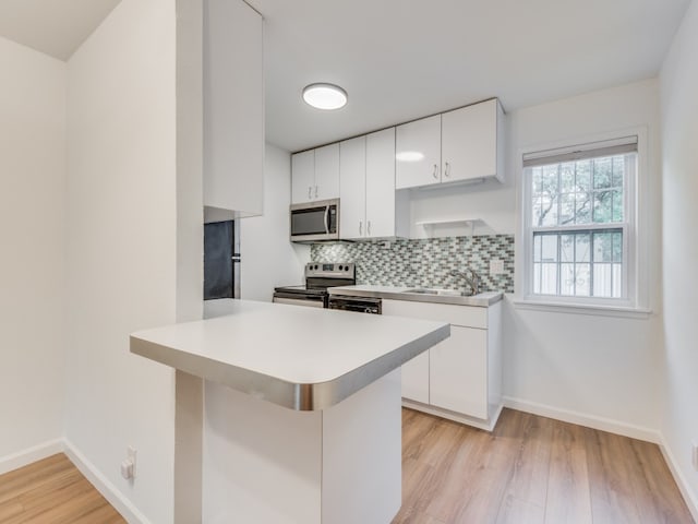 kitchen with light hardwood / wood-style floors, white cabinetry, backsplash, kitchen peninsula, and stainless steel appliances