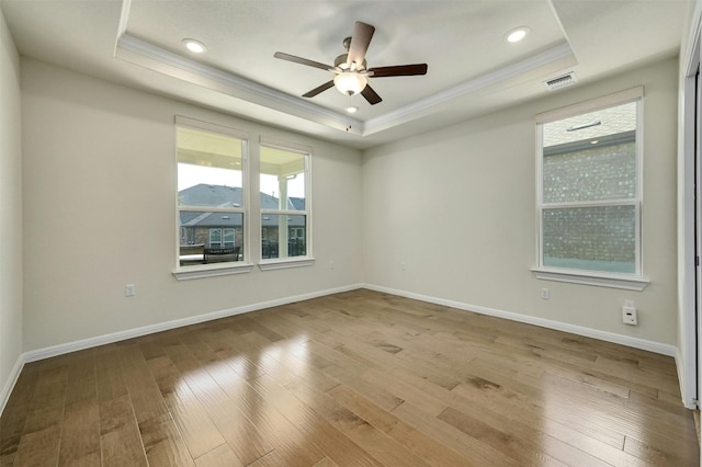 empty room with a tray ceiling, ceiling fan, light hardwood / wood-style floors, and crown molding