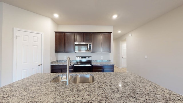 kitchen with dark brown cabinets, stainless steel appliances, light stone countertops, and sink