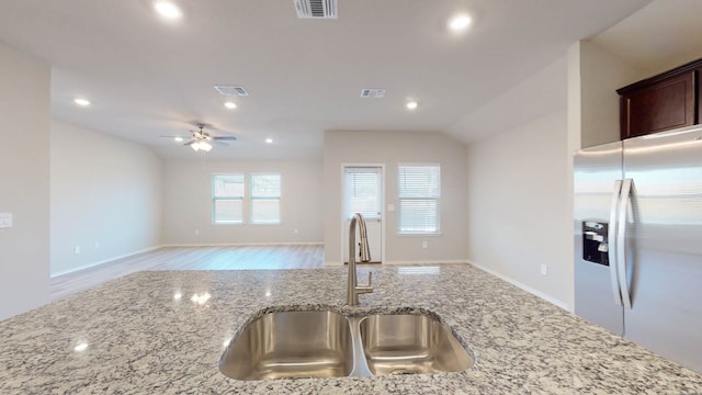 kitchen with ceiling fan, lofted ceiling, sink, stainless steel refrigerator with ice dispenser, and light stone countertops