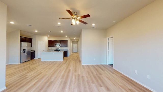 kitchen with ceiling fan, an island with sink, sink, stainless steel appliances, and light wood-type flooring