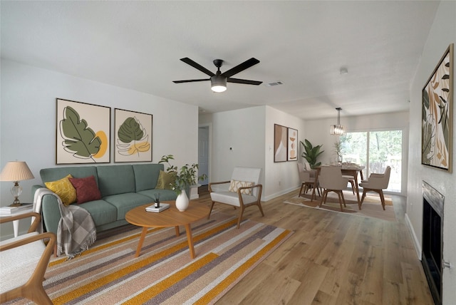 living room featuring ceiling fan with notable chandelier and light hardwood / wood-style flooring