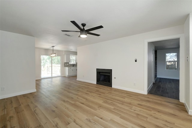 unfurnished living room with ceiling fan with notable chandelier, sink, and light hardwood / wood-style flooring