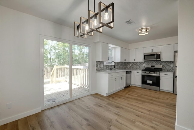 kitchen with sink, white cabinetry, hanging light fixtures, light hardwood / wood-style flooring, and stainless steel appliances