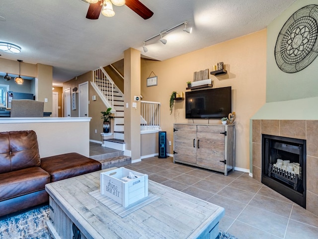 living room with ceiling fan, a textured ceiling, tile patterned flooring, and a tile fireplace