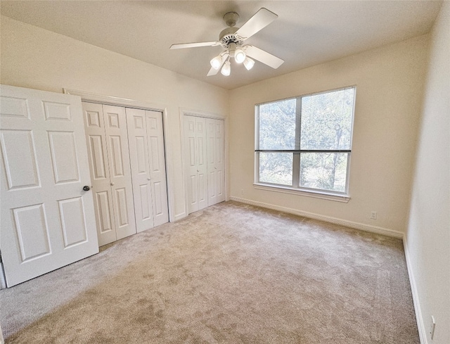 unfurnished bedroom featuring two closets, light carpet, and ceiling fan