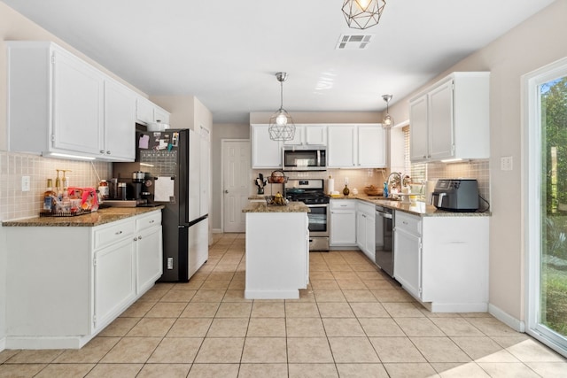 kitchen with dark stone counters, appliances with stainless steel finishes, decorative light fixtures, a kitchen island, and white cabinetry