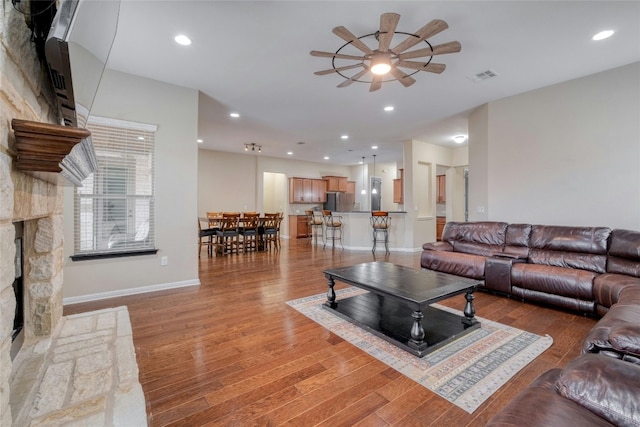 living room featuring wood-type flooring, ceiling fan, and a stone fireplace