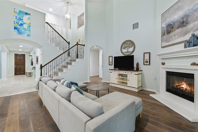 living room with a towering ceiling, a chandelier, and dark wood-type flooring