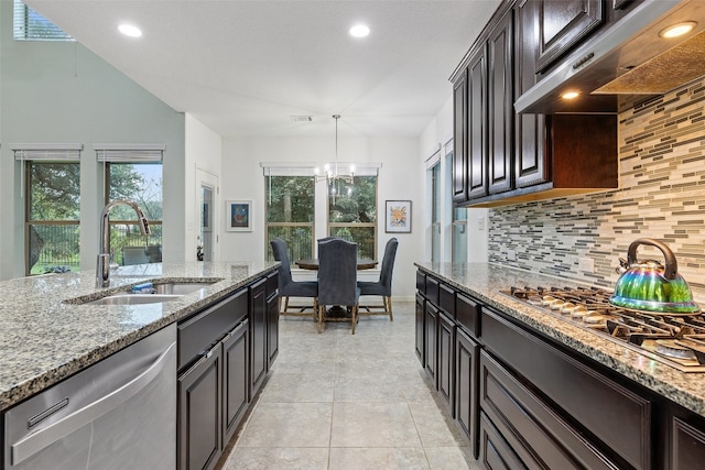 kitchen featuring appliances with stainless steel finishes, light stone counters, backsplash, sink, and a notable chandelier