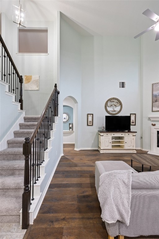 living room featuring ceiling fan with notable chandelier, a towering ceiling, and dark wood-type flooring