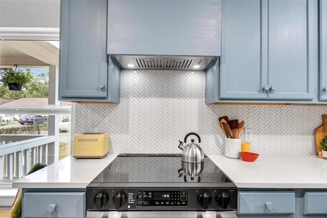 kitchen featuring electric stove, backsplash, blue cabinetry, and custom range hood