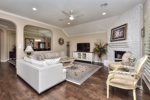 living room featuring lofted ceiling, ornamental molding, a stone fireplace, dark wood-type flooring, and ceiling fan with notable chandelier