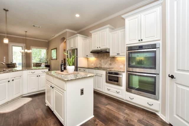 kitchen with pendant lighting, dark wood-type flooring, stainless steel appliances, a center island, and a notable chandelier