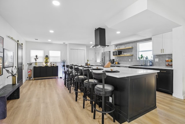 kitchen with sink, light hardwood / wood-style flooring, a kitchen island, stainless steel fridge with ice dispenser, and island exhaust hood