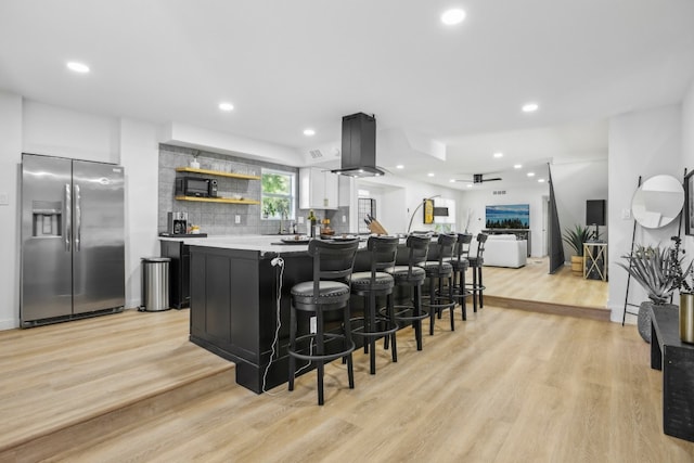 kitchen with white cabinets, light wood-type flooring, tasteful backsplash, stainless steel fridge with ice dispenser, and island exhaust hood