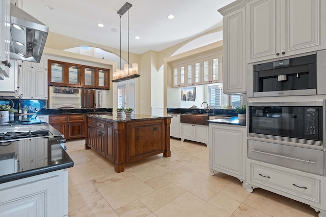 kitchen with white cabinetry, black microwave, a center island, ventilation hood, and decorative light fixtures