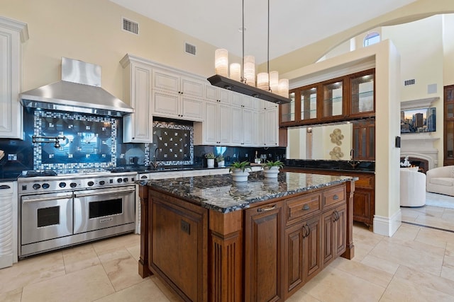 kitchen featuring a kitchen island, dark stone countertops, decorative backsplash, double oven range, and wall chimney exhaust hood