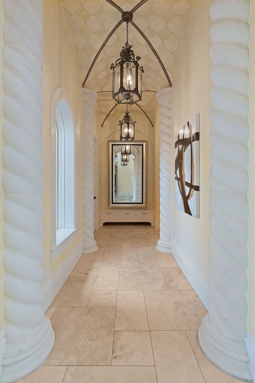 hallway with ornate columns, lofted ceiling, and a notable chandelier