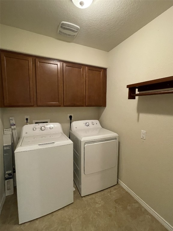 laundry area with washer and clothes dryer, cabinets, and a textured ceiling