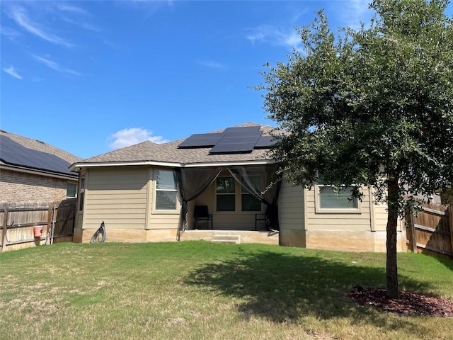 rear view of property featuring a yard and solar panels