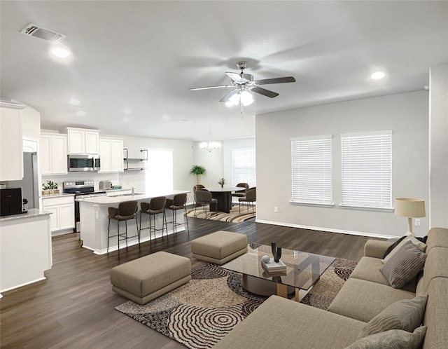 living room with ceiling fan with notable chandelier, sink, and dark wood-type flooring