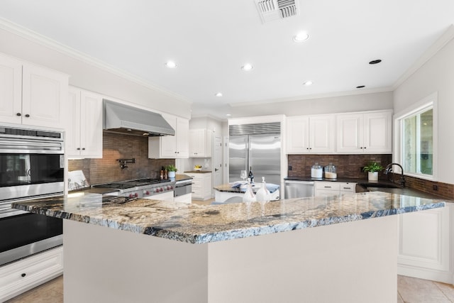 kitchen featuring wall chimney exhaust hood, a center island, stainless steel appliances, and white cabinets