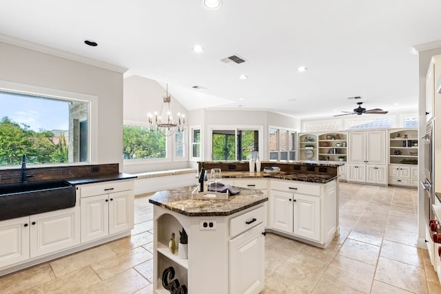 kitchen with ceiling fan with notable chandelier, dark stone countertops, white cabinetry, and a center island